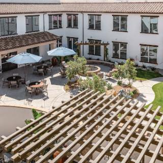 A beautifully designed courtyard featuring a patio with umbrellas, surrounded by lush greenery and modern architecture.