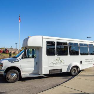 A white shuttle bus parked outdoors under a clear blue sky.