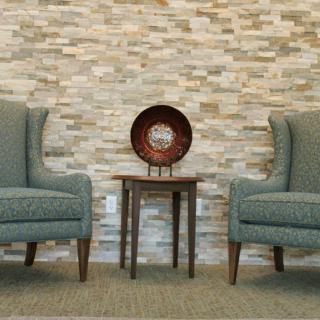 A stylish living room setup with two armchairs flanking a small wooden table against a stone wall backdrop.