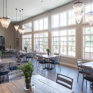 A bright and modern restaurant interior featuring large windows, elegant chandeliers, and neatly arranged tables and chairs.