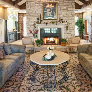 A cozy, traditionally styled living room featuring a stone fireplace, elegant sofas, and a decorative coffee table.