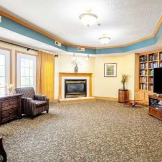 A cozy living room with a fireplace, armchair, television, and large windows.