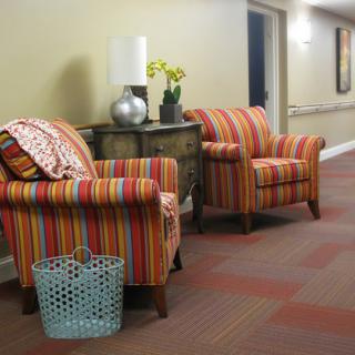 A cozy hallway with striped armchairs and a small table decorated with flowers and a lamp.