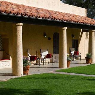 A beautiful house with a shaded porch, featuring columns and comfortable patio seating, overlooks a lush green lawn.