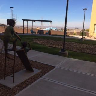 A sculpture of a person on a bench in an outdoor park setting with walkways and distant landscape views.