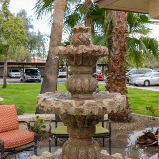 A garden scene featuring a multi-tiered stone fountain surrounded by palm trees and patio seating.