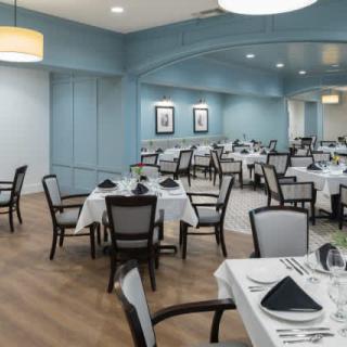 An elegant restaurant dining room with neatly arranged tables and chairs, set with white tablecloths and folded napkins.