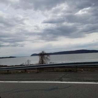 A serene lakeside view under a cloudy sky, captured from the roadside.