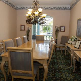 A formal dining room featuring a large wooden table, elegant chandelier, and decorative plants.