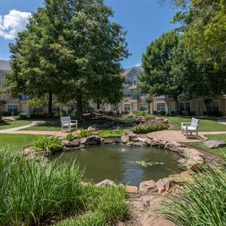 A serene garden with a pond and benches, surrounded by lush greenery and trees.