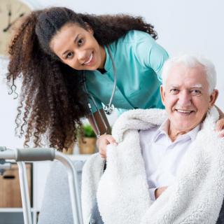 A nurse assisting a senior citizen with a warm smile and a blanket.