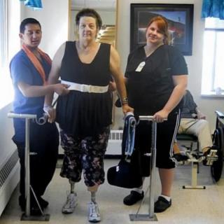 A patient undergoing physical therapy with the support of two healthcare professionals.