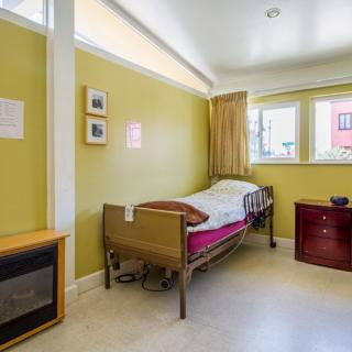 A simple hospital room with yellow walls, featuring a bed and a window.
