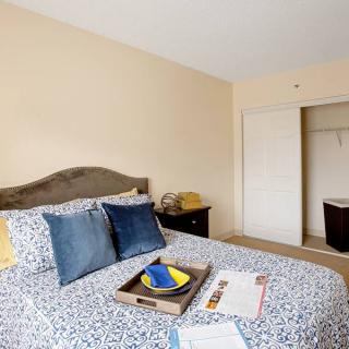 A cozy bedroom with a neatly made bed, featuring decorative pillows and a tray on top. There's a dresser beside the bed and an open closet in the background.