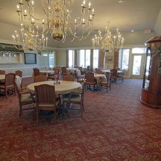 An elegant dining room featuring chandeliers, round tables with chairs, and a patterned carpet.