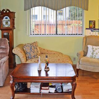 A cozy living room with a wooden coffee table, armchair, and chaise lounge, featuring a grandfather clock by the window.
