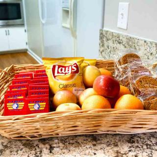 A basket on a kitchen counter filled with assorted snacks, fruits, and granola bars.