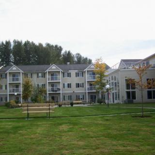 A residential apartment complex with a spacious lawn and trees in the background.