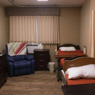 A cozy nursing home room with two beds and a recliner chair.