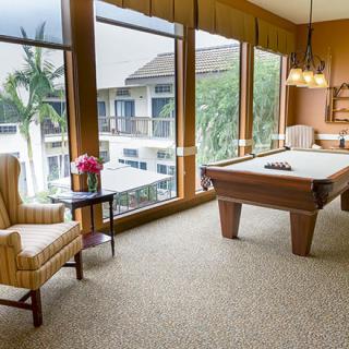 A well-lit game room featuring a billiards table, comfortable seating, and large windows with a view.