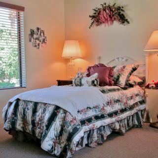 A cozy bedroom featuring floral bedding, warm lighting from two lamps, and a window with blinds.