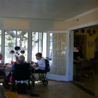 A group of seniors gathered around a table in a bright dining area with large windows.