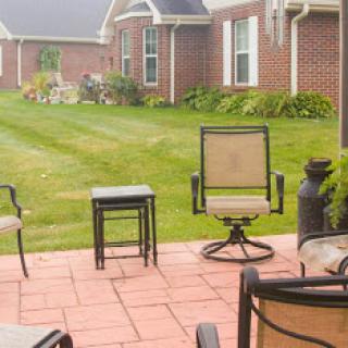 A cozy outdoor patio set up with chairs and a small table, surrounded by lush green grass and a brick home.