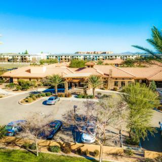 Aerial view of a building complex with a parking lot surrounded by desert landscape and trees.