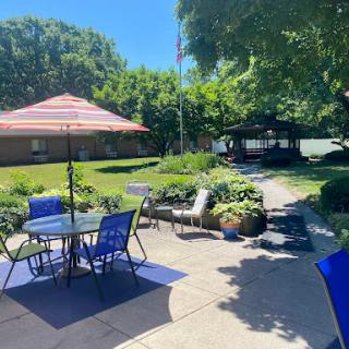 A bright and inviting outdoor patio area with seating, a colorful umbrella, and lush greenery.