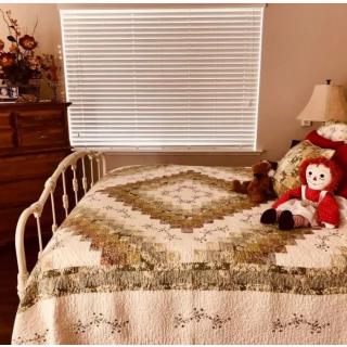 A cozy bedroom with a vintage quilt and dolls on the bed.