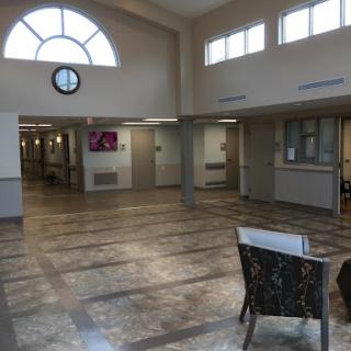 A spacious hospital lobby featuring a seating area, large windows, and a clock on the wall.