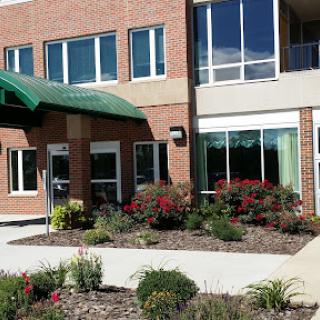 A modern brick building with large windows and a welcoming entrance, surrounded by colorful flowers.