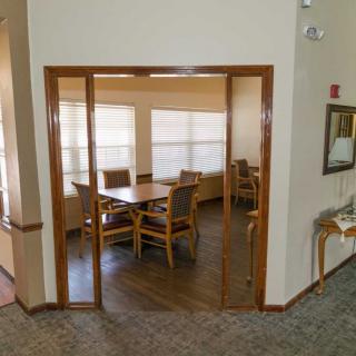 A cozy dining area with a wooden table and chairs, illuminated by natural light from large windows.