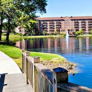 A serene view of a lake surrounded by lush greenery and a residential building reflecting on the water's surface.