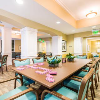 A well-lit dining room with a large table and multiple chairs, featuring modern decor and ample seating.