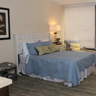 A beautifully designed bedroom featuring a comfortable bed with blue bedding, decorative pillows, and a stylish lamp beside the window.