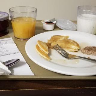 A breakfast spread featuring pancakes, sausage, orange juice, and milk served on a meal tray.