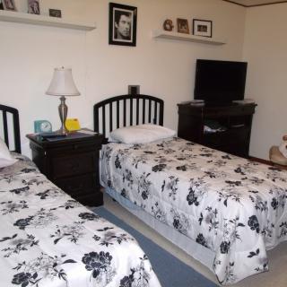 A cozy bedroom with twin beds featuring floral bedding, a nightstand with a lamp, and a television on a dresser.
