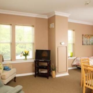A cozy living room with beige walls, featuring a television, comfortable furniture, and large windows.