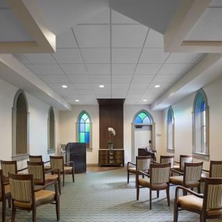 A small chapel interior with seating arrangements and arched windows.