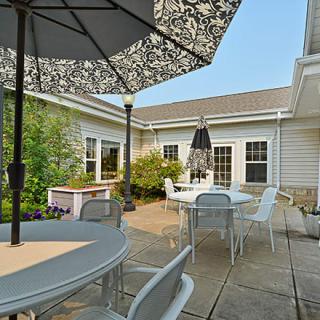 A cozy backyard patio with tables, chairs, and umbrellas surrounded by greenery.