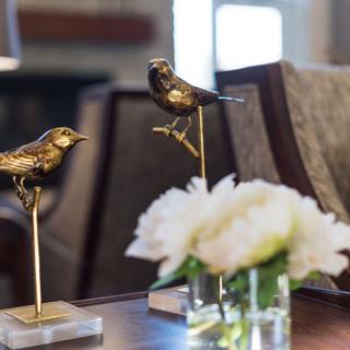 Bronze bird sculptures perched elegantly on a table alongside a white flower arrangement.