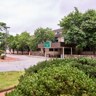 A view of a building surrounded by green trees and shrubbery, with a road sign visible in the foreground.