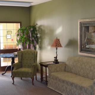 A cozy living room featuring a sofa, armchair, and table with a lamp, decorated with a potted plant and wall art.