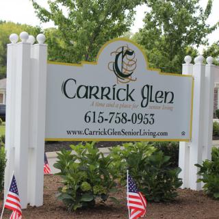 Entrance sign for Carrick Glen with contact information and American flags.