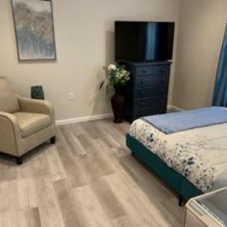 A cozy bedroom featuring a bed with floral bedding, a TV on a dresser, and a comfortable chair.