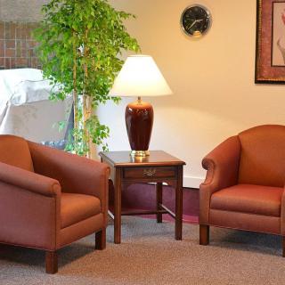 A cozy seating area with two armchairs, a lamp on a wooden table, and a potted plant.