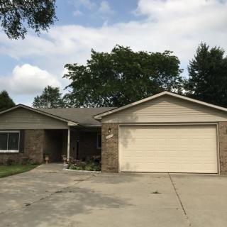 A single-story suburban house with a two-car garage and a driveway, surrounded by trees under a cloudy sky.