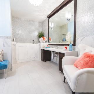 A modern and elegantly designed bathroom featuring a large mirror, a white chair with a coral pillow, and a sleek vanity area.