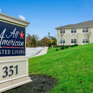 Entrance sign of All American Assisted Living with a view of the facility and surrounding greenery.